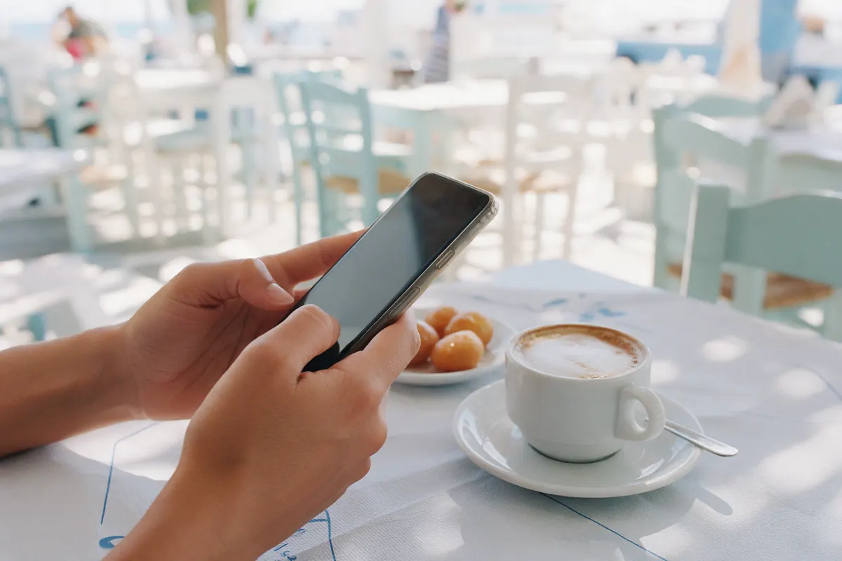 A phone and a coffee on a sunlit café table.