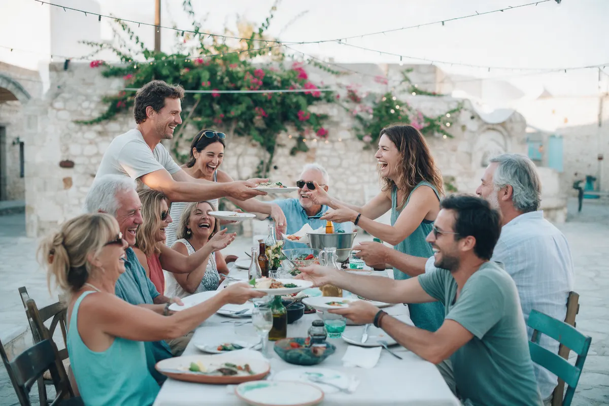 Friends share a long table at an outdoor community dinner in a village square.